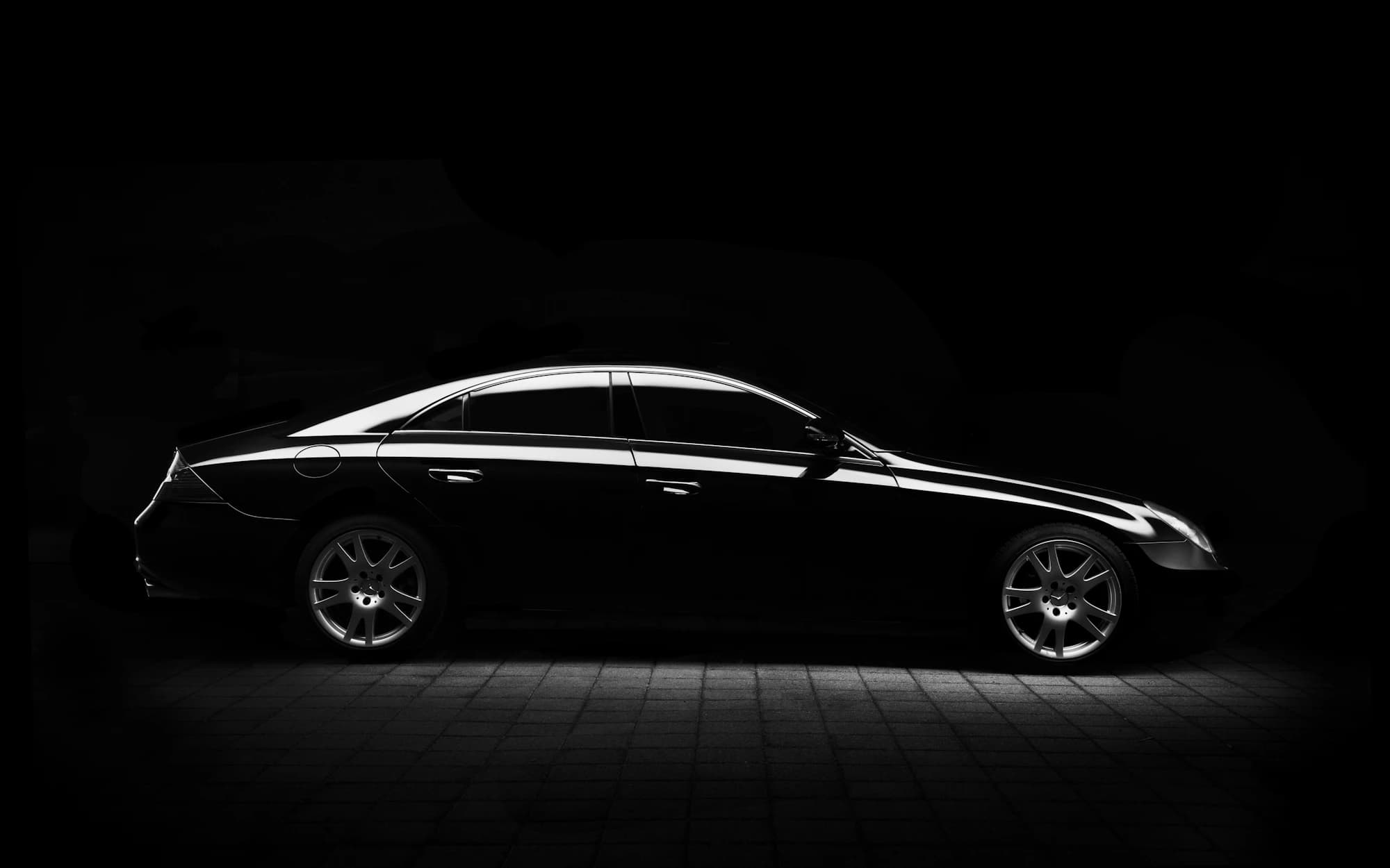 A black coupe under a single light in a dark garage